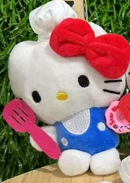 Hello kitty plišani privjesak bijela plišana lutka u plavim hlačicama i kuhinjskom kapom drži ružičastu lopaticu