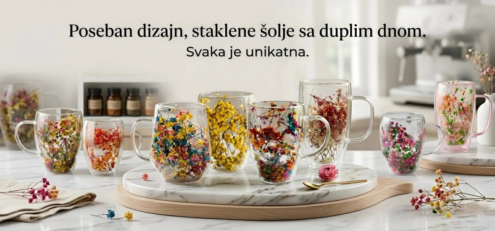 Jasne šalice od dvostrukog stakla ispunjene šarenim suhim cvijećem, svaka jedinstveno dizajnirana i prikazana na mramornoj podlozi.