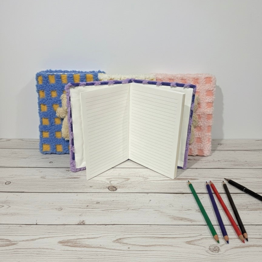 Plavi i žuti kvačkani Medo rokovnik A5 otvoren na bijeloj drvenoj površini