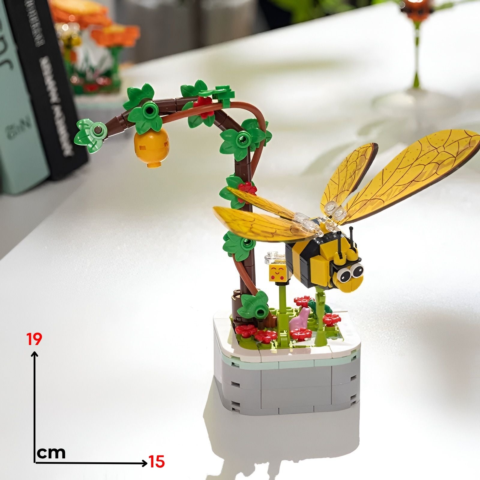 Žuta i crna lego mala pčela s prozirnim krilima na minijaturnom stablu s zelenim lišćem crvenim cvijećem i narančom